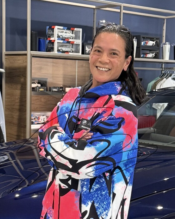 Tona E Zarrelli smiling, arms folded, in a jacket patterned with bold pink, blue and white abstract shapes.